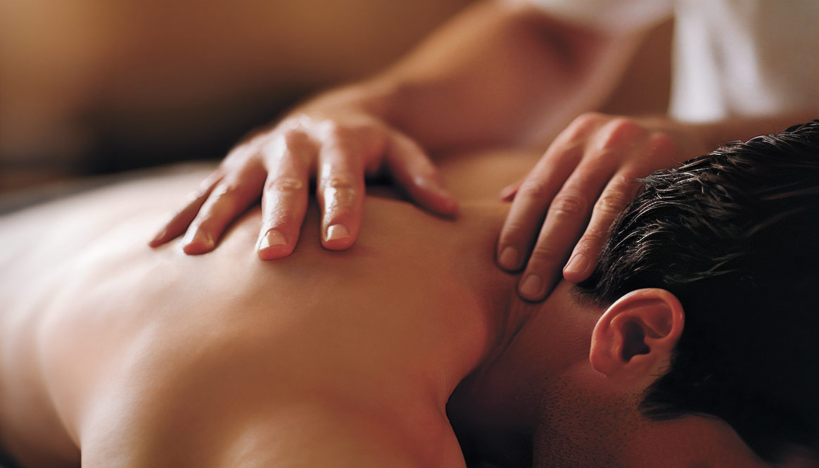 Hands massaging the back of a man laying on a massage table.